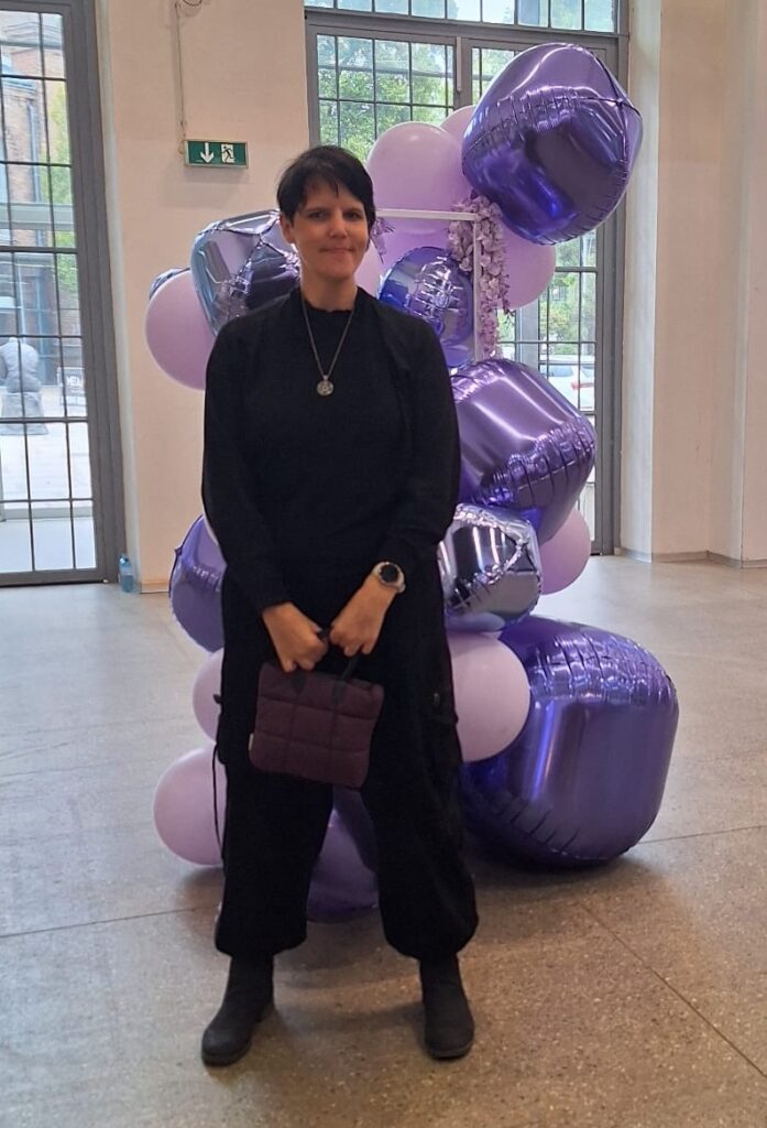 Karoline steht vor lila und rosa Luftballons.
